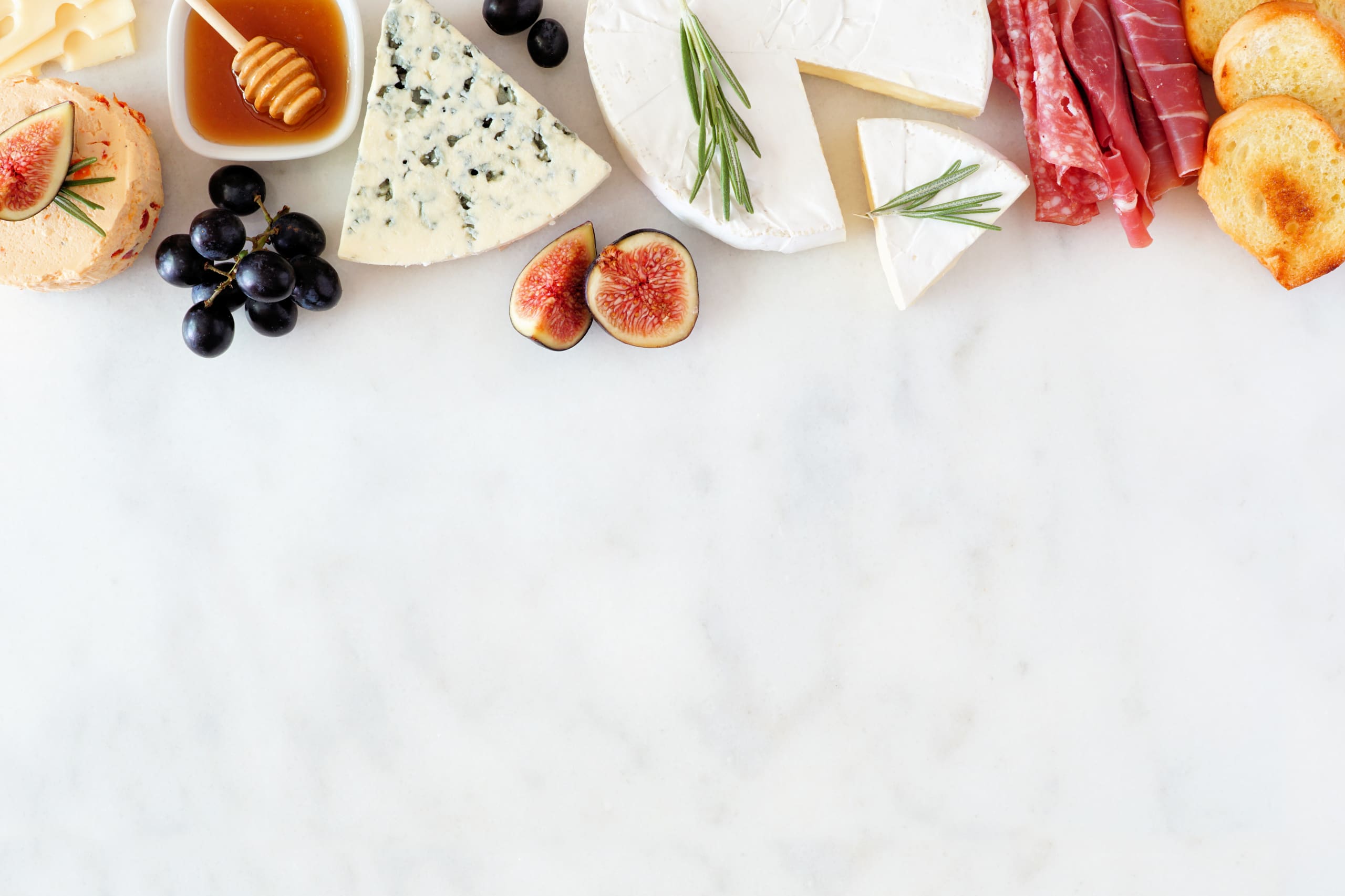 Assorted cheeses and meat appetizers. Top border, overhead view on a white marble background. Image represents Compassion's You Version plan Are you Hungry?