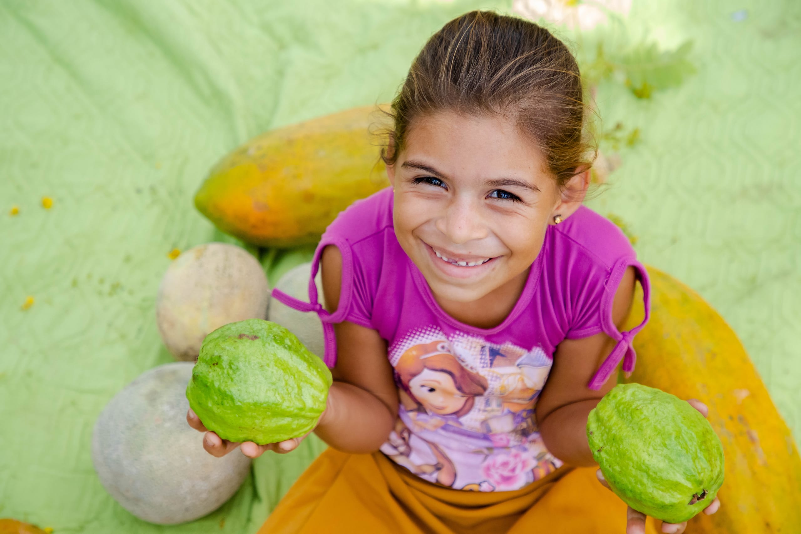 Girls wears a pink shirt and holds vegetables in her hands.