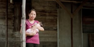 A mother stand on a covered patio in front of her home, holding a new born baby.
