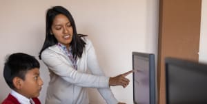 A female teacher teaching a young boy how to use a computer.