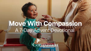 A toddler is sitting upright on a table while her mother reaches out to her. Overlaying the photo is the title "Move With Compassion" with the subtitle "A 7-Day Advent Devotional".