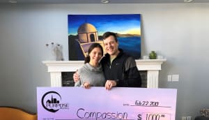 Man and woman smile, holding a cheque for Compassion.