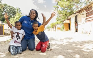 Sugeli, an administrative assistant at a Dominican Republic Compassion centre, poses with two boys on the street. They are kneeling and smiling while throwing their hands up.