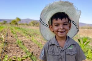 Little boy smiles big wearing a hat standing in a garden