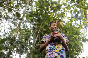 Waira, a 12-year-old boy in Ecuador, is standing in the jungle laughing and holding a plant.