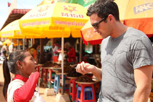 A man in sunglasses and a grey shirt talks with a girl in red and white