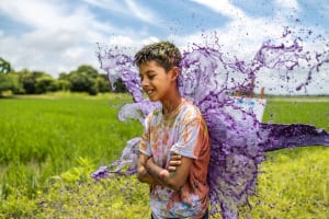 Boy standing as purple paint is poured at him.