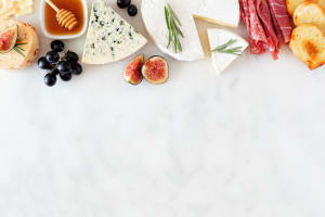 Assorted cheeses and meat appetizers. Top border, overhead view on a white marble background. Image represents Compassion's You Version plan Are you Hungry?