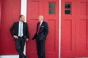 Ian Ardill stands in a dark suit with briefcase against a large red door.