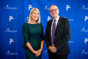 Allison and Barry pose in front of a blue Compassion backdrop.