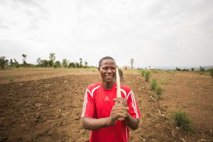 A man stands in a freshly tilled field, a garden hoe resting on his shoulder.