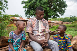 An older black man smiles as he sits beside two happy kids