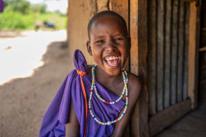 A girl in a purple dress and beaded necklace laughs.