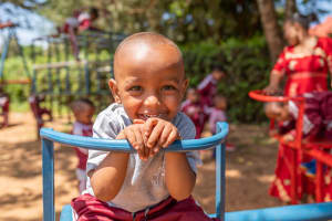 A little boy in a grey shirt sits on a blue seat on the playground.