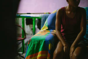 A woman sits on a bed, looking away.