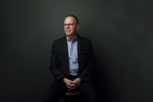 a portrait of Barry. He is wearing a blue shirt and black blazer, sitting and looking into the distance.