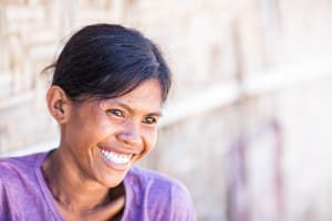 A woman wearing a purple shirt, smiles looking up and off to the side in a close-up portrait.