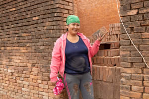 A woman in a pink hoodie and green bandana stands in front of a stack of bricks.