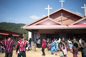 People mill about in front of a church with three crosses on it's steeples.