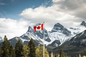 Mountains and trees with a Canadian flag on a pole.