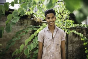 Shanto stands amidst green leaves in a plaid shirt and smiles.