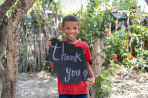A Colombian boy named Franklin is smiling and holds up a sign that says "thank you!"