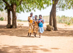 Three girls in dresses stand between two trees holding open books.