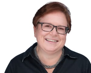 A woman in glasses and a black shirt smiles at the camera