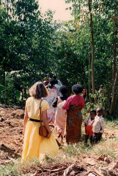 Two young Rwandan boys stand beside a forest trail as visitors and locals walk by.