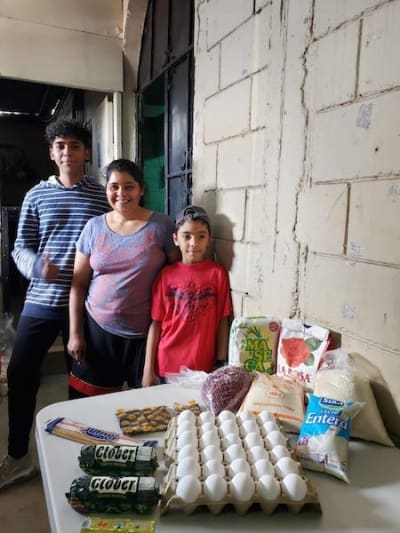 A family poses in front of a table of groceries delivered by Compassion staff.