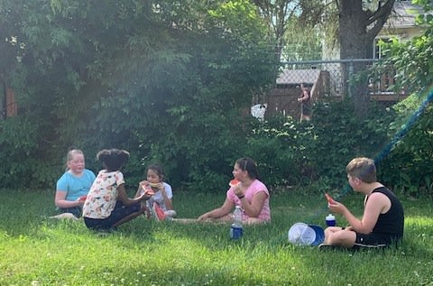 Kids sit on the grass eating watermelon