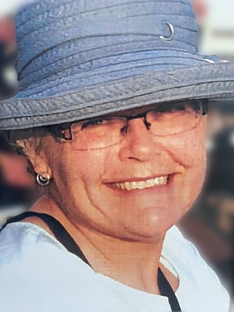 A close-up picture of Gail. She is wearing glasses, smiling and wearing a blue sunhat.
