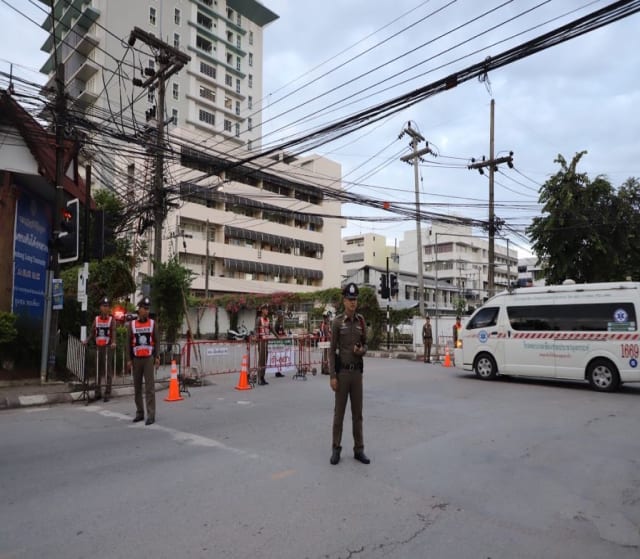 A policeman is pictured in the middle of the street. Behind him is a small bus and some tall buildings.