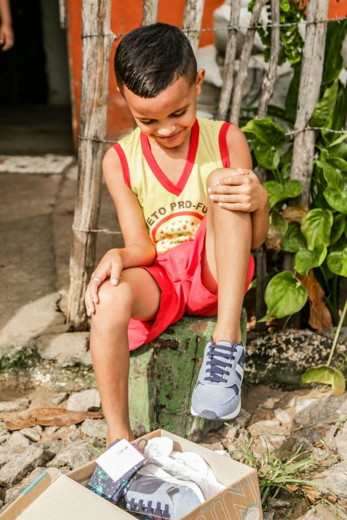 Little boy wearing a jersey looks down with a smile at his new blue running shoes.