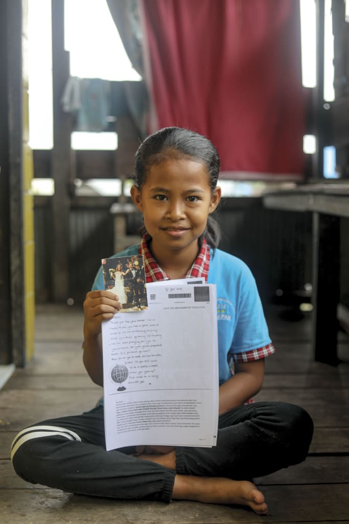 10 year-old girl sits on her floor smiling with a letter and picture from her sponsors.