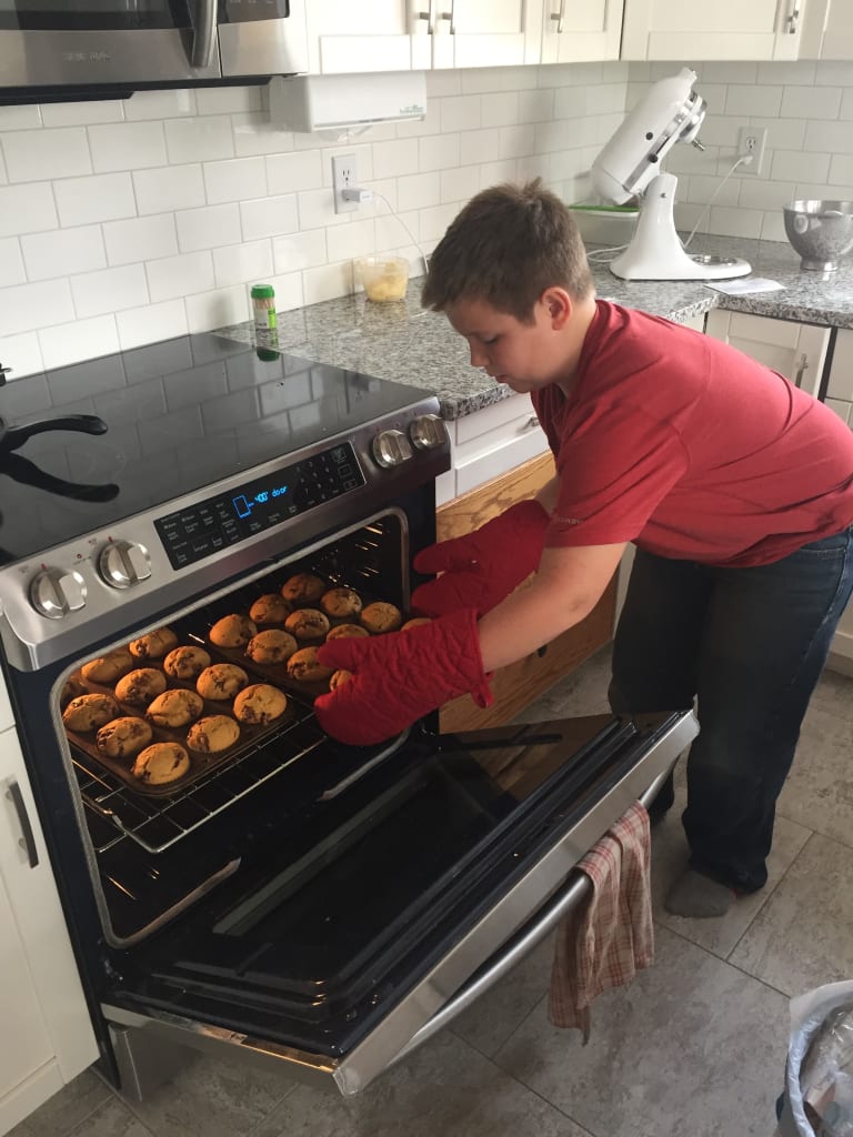 Jacob wears a red t-shirt and puts his muffins in the oven.