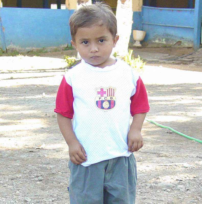 A young boy wears black dusty shoes, baggy grey pants and a white and red t-shirt.