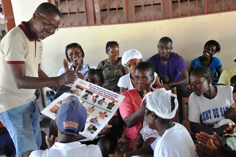 A man in glasses holds an infographic and teaches a group of caregivers.