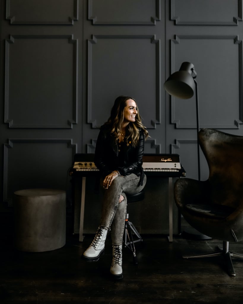 Brooke is pictured sitting by a piano in a black painted room.