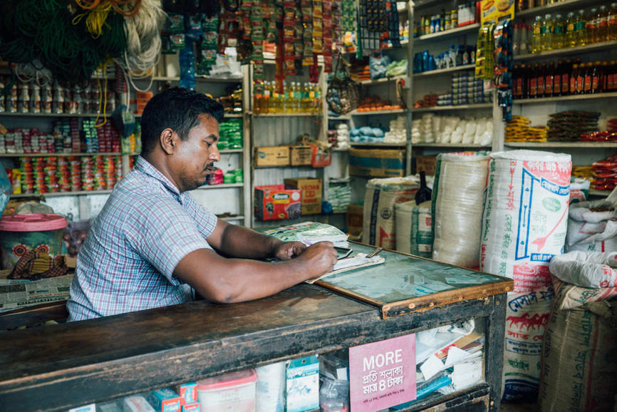Junaid, a local grocer in Bobita’s community, sits in his store and looks at some paperwork.