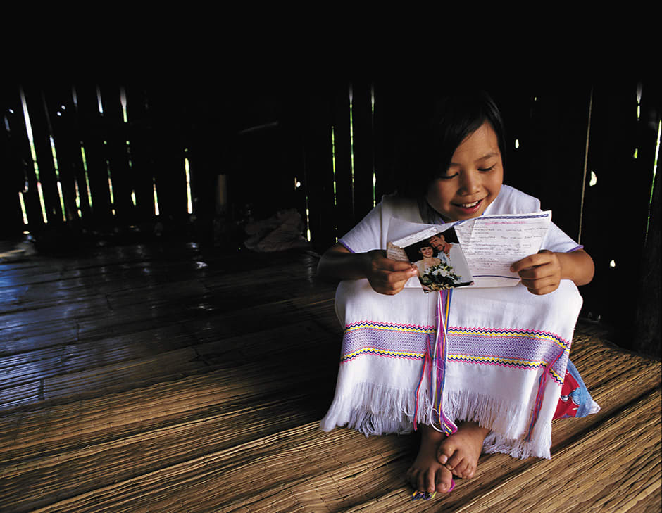 A young girl in white sits on a wood floor and reads a letter.